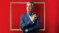 Actor Andrew McFarlane in a promotion image for David Williamson's The Social Ladder', which opens Ensemble Theatre's 2026 season. The actor, a dapper, tanned man with grey hair, wears a suit, shirt and cravat, and is posing before an ornate gilded picture frame against a bright red background.