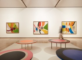Gallery view of an exhibitio with colour abstract paintings and round table sculptures. Janet Dawson