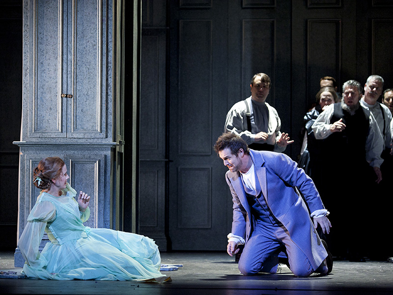 Sian Sharp as Olga and James Egglestone as Lensky in Opera Australia's 'Eugene Onegin' 2014. The production returns for the company's 2026 season. The photo depicts a young woman in period dress, sitting on the floor and seemingly recoiling from a kneeling man; a group of onlookers stand in the background.