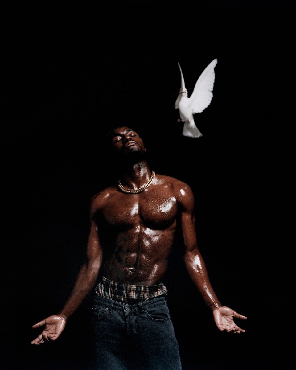 Dramatic photography of a man with dark skin and naked torso against black background. Photography festival