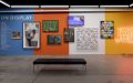 A gallery wall painted blue, orange, white and yellow (in that order) showcasing a series of different artworks at Artbank.