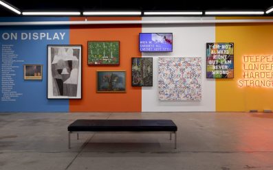 A gallery wall painted blue, orange, white and yellow (in that order) showcasing a series of different artworks at Artbank.