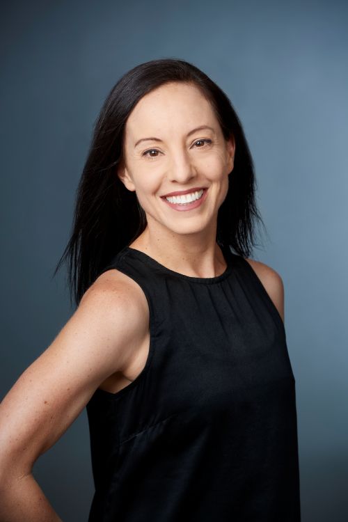 West Australian Ballet’s new Artistic Director Leanne Stojmenov. The photo depicts a fair skinned and lean older woman smiling at the camera. She has long black hair and wears a simple, sleeveless black dress.