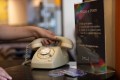 A hand on a rotary phone with a placard next to it saying 'Phone-a-Poem'. Taking Poetry off the Page.