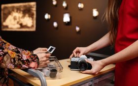 A close crop of two pairs of hands holding a camera and some film inside a photography exhibition. Free exhibitions in Queensland.