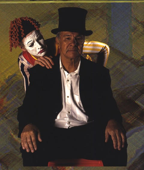 A promotional photo of Noel Tovey in character in the Fruities' 2004 production 'Skipping on Stars'. Photo: Flying Fruit Flies Circus. Uncle Noel wears a black suit and an open white whirt, with no tie, and a black top hat on his head. A frowning clown poses behind him, its right hand on his right shoulder.