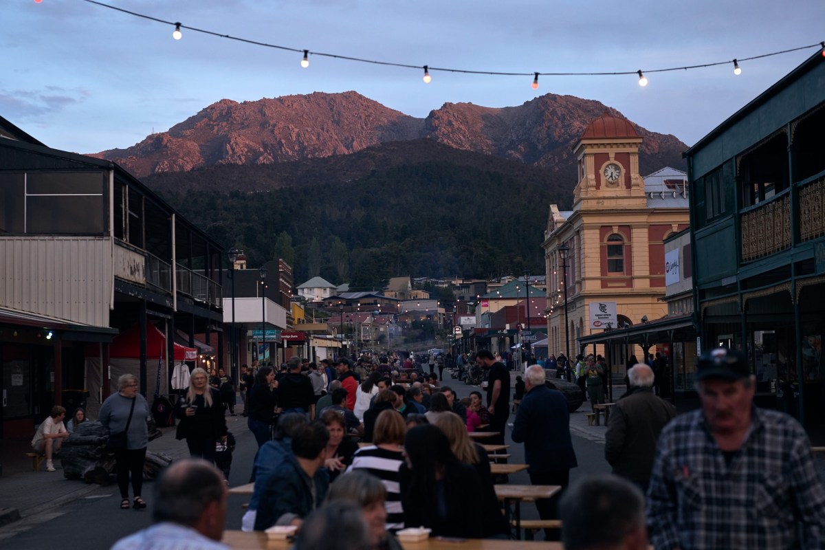 Image of a crowd in the street in a regional town in Australia at dusk with old buildings and mountains. The Unconformity