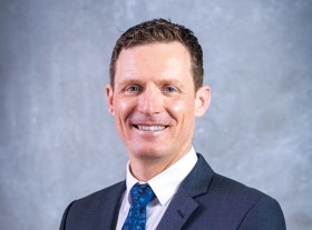 A profile photo of a man with brown hair, a dark suit and blue tie. He is smiling. Michael Sterzinger, CEO of Queensland Symphony Orchestra. QSO