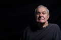 A promotional photograph of the late Noel Tovey AM from the 2014 season of 'Little Black Bastard', presented by ILBIJERRI and Arts House. The photo shows an elder but still vigorous Aboriginal man with grey hair; he poses regally and is looking gravely down at the camera.