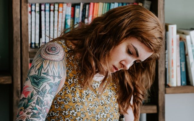 A figure with curly red hair and tattooed arm looking down. Opportunities and awards.