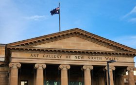 The exterior building of the Art Gallery of New South Wales, a colonial sandstone structure with the Australian flag flying on top. AGNSW.