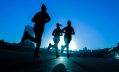 A moody photograph, taken at a low angle, showing three jogging women in the early morning. The women are silhouetted against the cool blue sky and their shadows stretch behind them on the road as they run towards the soon-to-rise sun which lightens the background of the photo. The image illustrates ArtsHub's weekly round-up of Australian arts sector appointments.