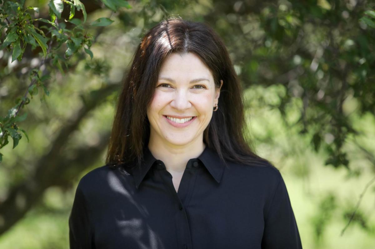 A brunette woman wearign a black top against foliage, Jessica Mansour-Nahra, author of The Farm.