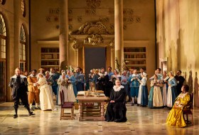 The cast of The Marriage of Figaro in costume in a large hall.