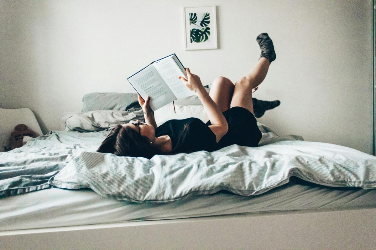 A woman lying on a bed reading a book. Best new books published October 2025 in Australia.