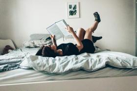 A woman lying on a bed reading a book. Best new books published October 2025 in Australia.