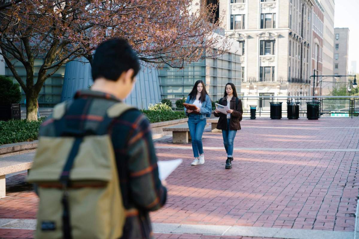 arts students: A photo of two young female university students walking while carrying their books in an open walkway on a university campus.