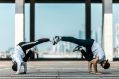Two male breakdancers perform on a high building, the cityscape visible behind them. The two young men are photographed in joint handstands; with their legs extended, their feet touching as if supporting one another. The photo illustrates Artshub's On the move column, a weekly summary of Australian arts sector appointments.