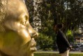 Girl with hair pulled back and dark skin looking at gold sculpture in her likeness.