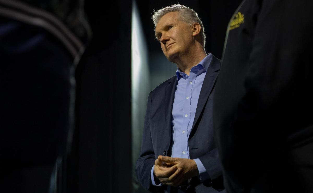 Federal Arts Minister Tony Burke: a middle aged white man with grey hair wearing a suit standing spotlight against a dark background. In this article, Burke discusses arts policy and Revive.