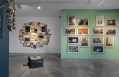 Exhibition view with painted green wall, photographs and jewelry. Helen Britton
