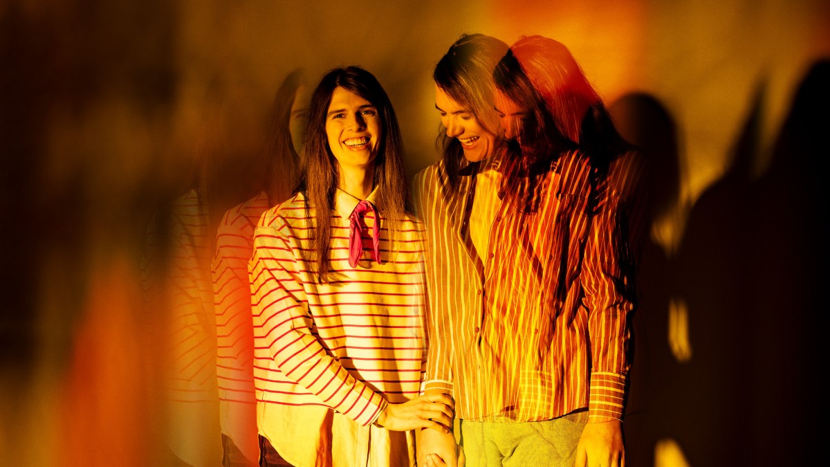 Publicity image for Griffin's 2026 production 'Afterglow', to be staged at Belvoir's downstairs theatre. Two fair-skinned young women with long hair, one wearing vertical striped clothes and the other wearing horizontal stripes, hold each other and laugh. The image is slightly fractured as if double-exposed, and shot in tones of yellow and orange.