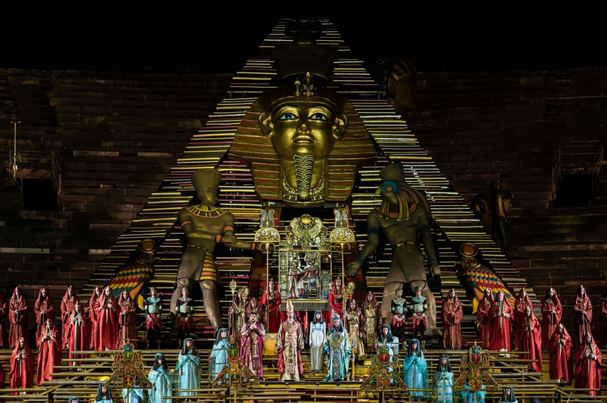 Franco Zeffirelli’s 'Aida' at Arena di Verona. The photograph hints at the scale of the arena production's opulent set, and depicts cast and chorus members arrayed beneath huge temple-like Egyptian statues and a pyramid.