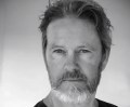 A recent 'Cluedo' publicity photo of actor Craig McLachlan. The black and white photo depicts a middle aged, fair skinned man with a neat grey beard and wearing a black t-shirt.