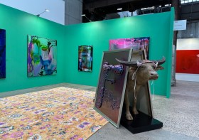 Image of a green art fair display with an ox holding up some paintings. Sydney Contemporary