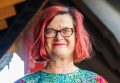 Image description: A photo of Fiona Winning, smiling at the camera. She has short red hair, glasses and is wearing a colourful green, pink and yellow top.