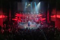 An orchestra and singers performing on stage with red lights shining from the sides.