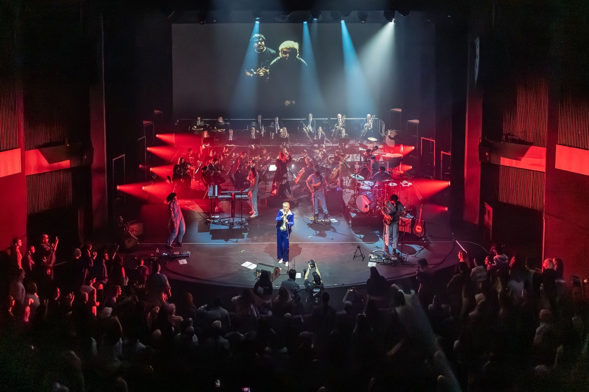 An orchestra and singers performing on stage with red lights shining from the sides.