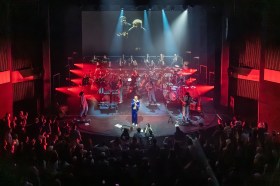 An orchestra and singers performing on stage with red lights shining from the sides.