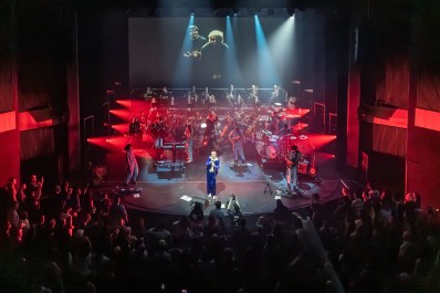 An orchestra and singers performing on stage with red lights shining from the sides.