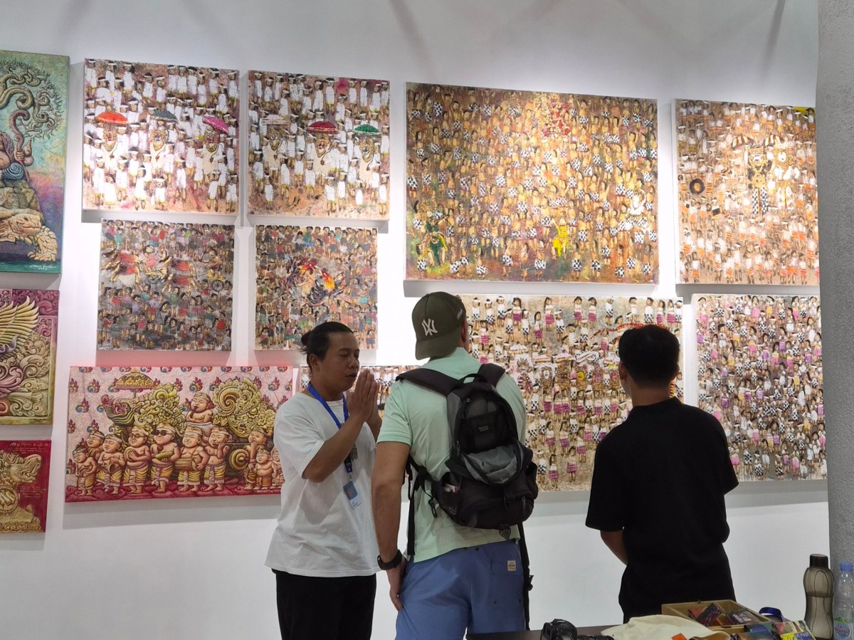 People interacting in front of a white booth filled with rows of paintings at Art&Bali 2025. 