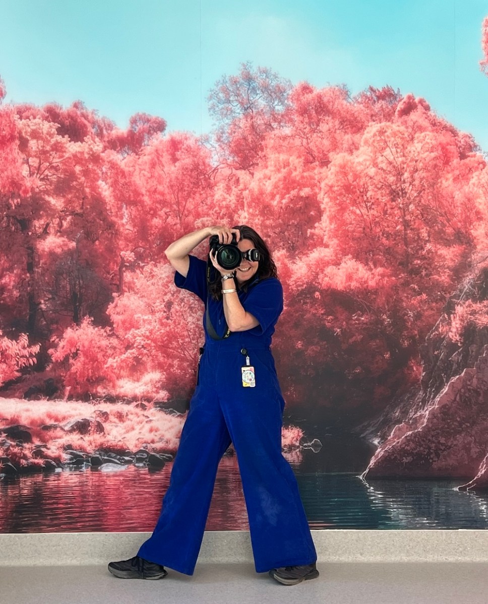 woman in blue jumpsuit taking a photograph with pink tree background. photojournalist 