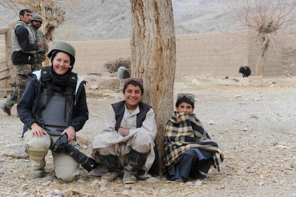 Women photojournalist wearing conflict protection with two boys in arid landscape. Photojournalist