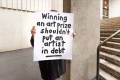 person holding a hand-written protest sign in front of their face. Tax Reform for the Arts