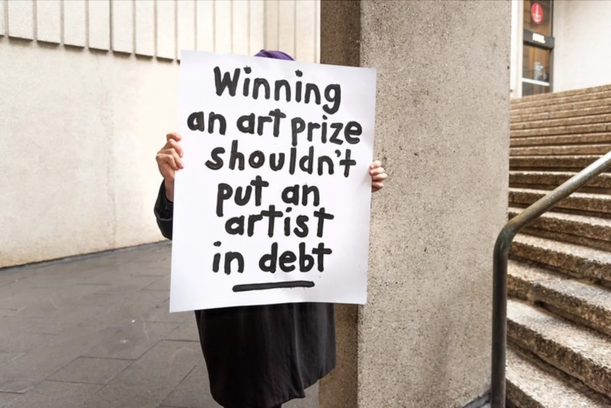 person holding a hand-written protest sign in front of their face. Tax Reform for the Arts