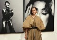 Women with dark hair wearing beige dress standing in front of black and white photographic portrait. Tina Arena