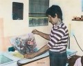 Miriam Stannage: an old looking coloured photograph of a woman at a kitchen holding a printed work on paper she has created.