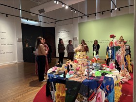Group of people in an exhibition with textiles listening to a talk. Analog Art Club