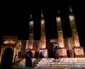 Two people in black standing on steps. There are big columns behind them in a production of Caesar.