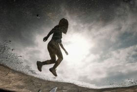 A jumping woman is reflected in the water of a lake or pond. The photo illustrates ArtsHub's weekly round-up of Australian arts sector appointments, On the Move.