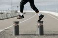 A close-up photograph of a person jumping from bollard to bollard on a stretch of road; the photo shows only their legs and feet. The person is wearing black pants, white socks and black and red sneakers. The photo illustrates Artshub's weekly On the Move column, which summarises the week's arts sector appointments across Australia.