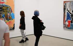 youth arts: a photo of two teenage girls standing in an art gallery space looking at two contemporary art paintings that hang on two different walls of the gallery.