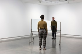 Art installation by Hany Armanious with mirror sculpture and man and woman facing each other reflected.