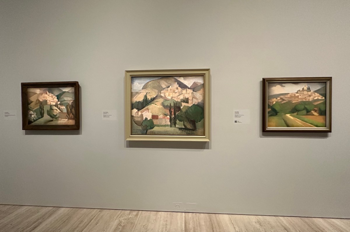 Installation view: Dangar, Black, and Grace Crowley, painted during a trip to the French village Mirmande in 1928, Art Gallery of NSW. Three modernist paintings of the same French landscape, each different in style though similar in colour and tone, hang on the grey gallery wall.