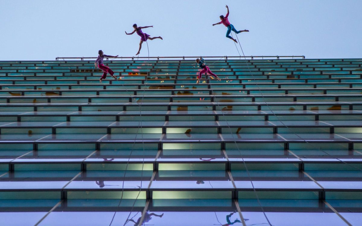 Dancers on the side of a tall building leaping.