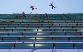 Dancers on the side of a tall building leaping.